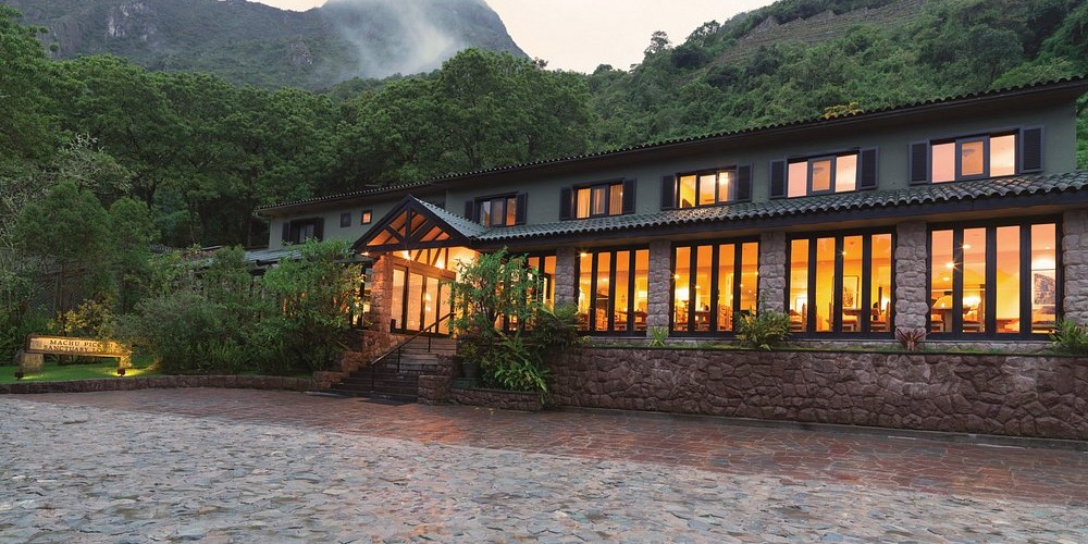 Belmond Sanctuary Lodge al atardecer: el edificio del lodge con el cerro y la vegetación detrás